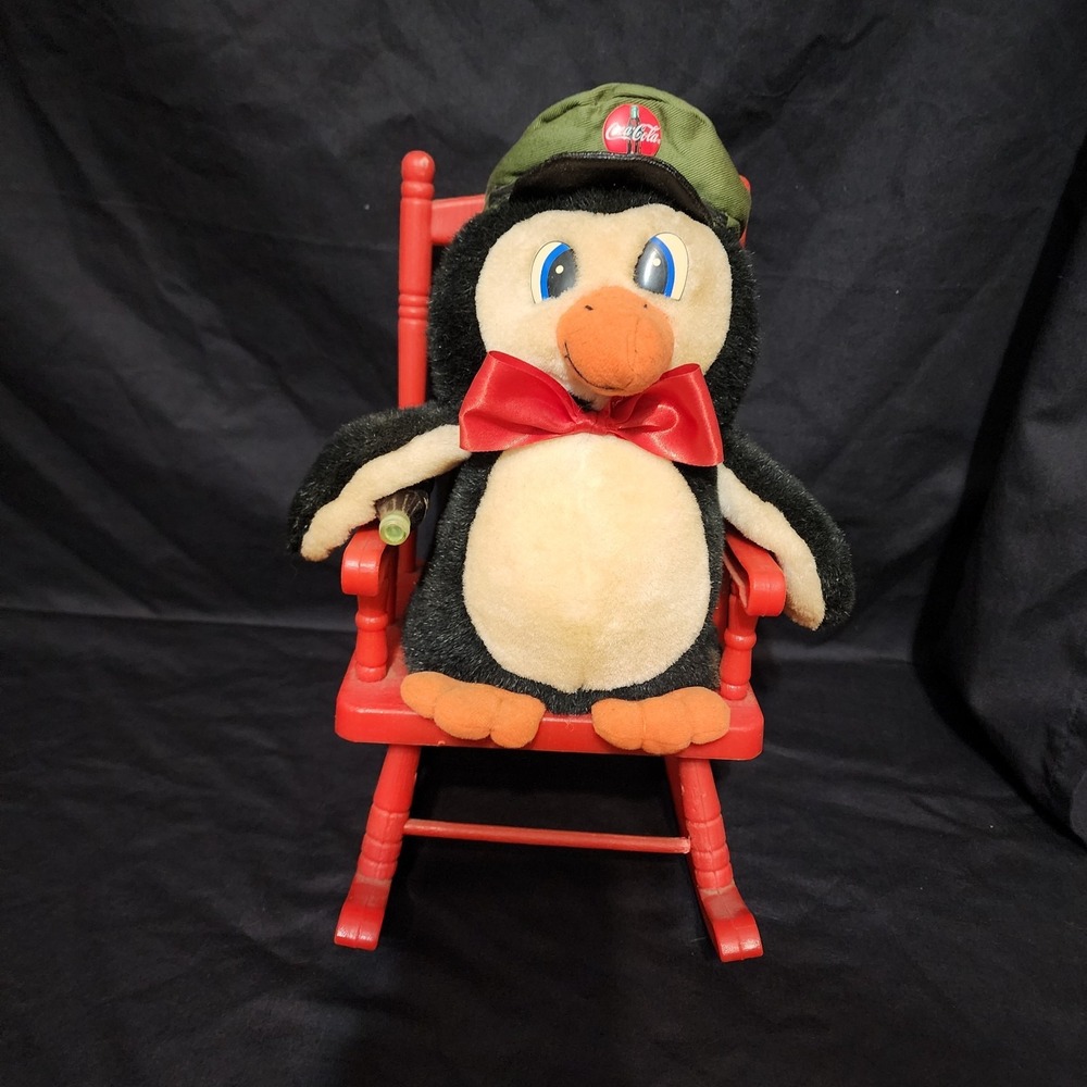 1997 vintage Coca-Cola penguin plush toy sitting in a red rocking chair.